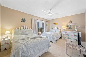 A bedroom with two beds, a ceiling fan, a dresser, and a window with curtains.