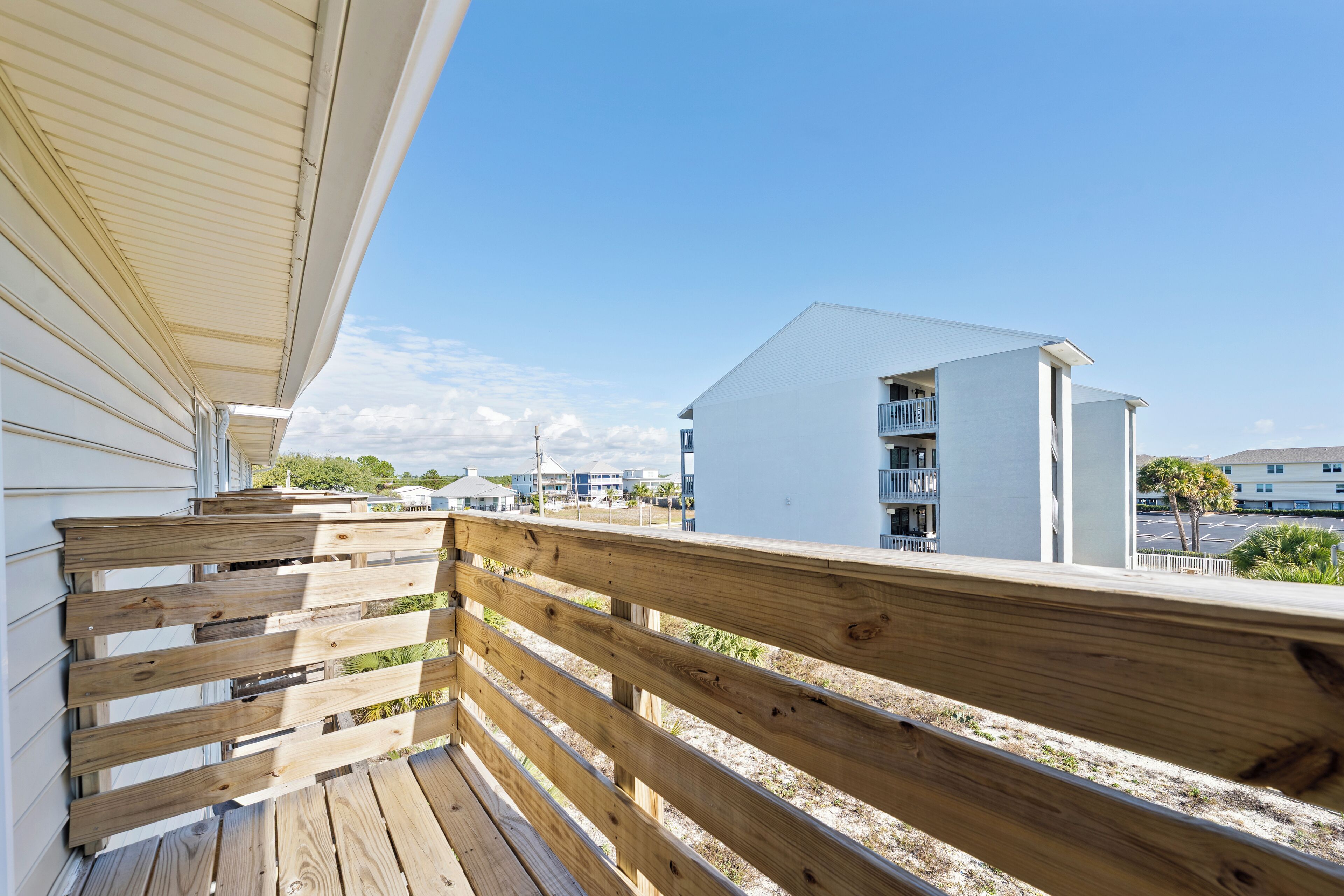 Una terraza de madera con barandilla, con vista a una zona residencial con casas y cielo despejado.