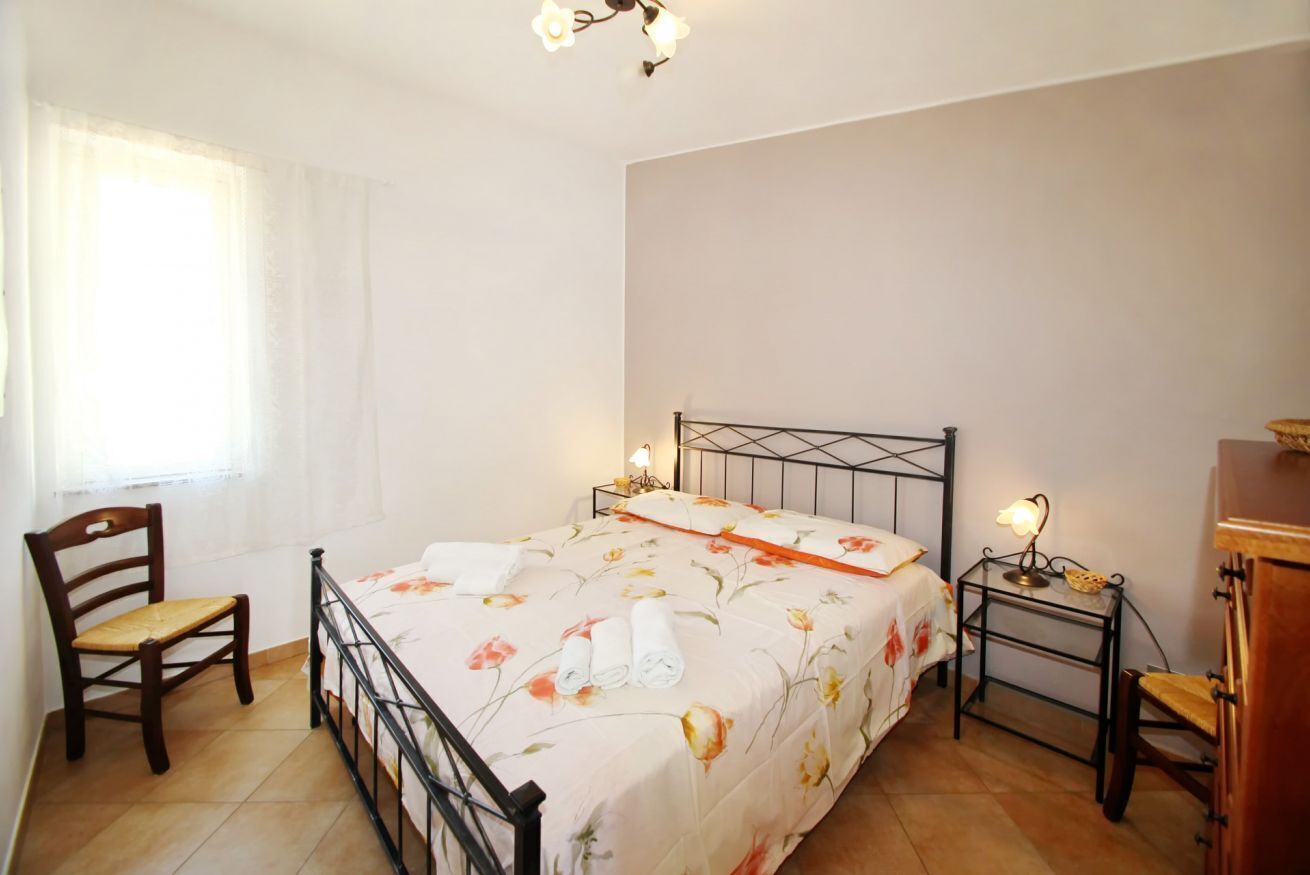 A bedroom with a bed, a chair, a nightstand, and a lamp.