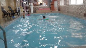 Una piscina al coperto con acqua cristallina, alcune persone che nuotano e una postazione di salvataggio sullo sfondo.