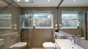 A modern bathroom with two toilets, a large mirror, and a glass shower enclosure. - Lovely 2 bed Flat With Garden in Queen's Park (London)