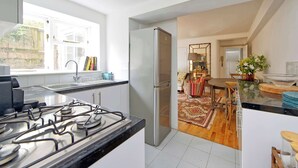 A modern kitchen with a stainless steel refrigerator, a gas stove, and a window providing natural light. - Lovely 2 bed Flat With Garden in Queen's Park (London)