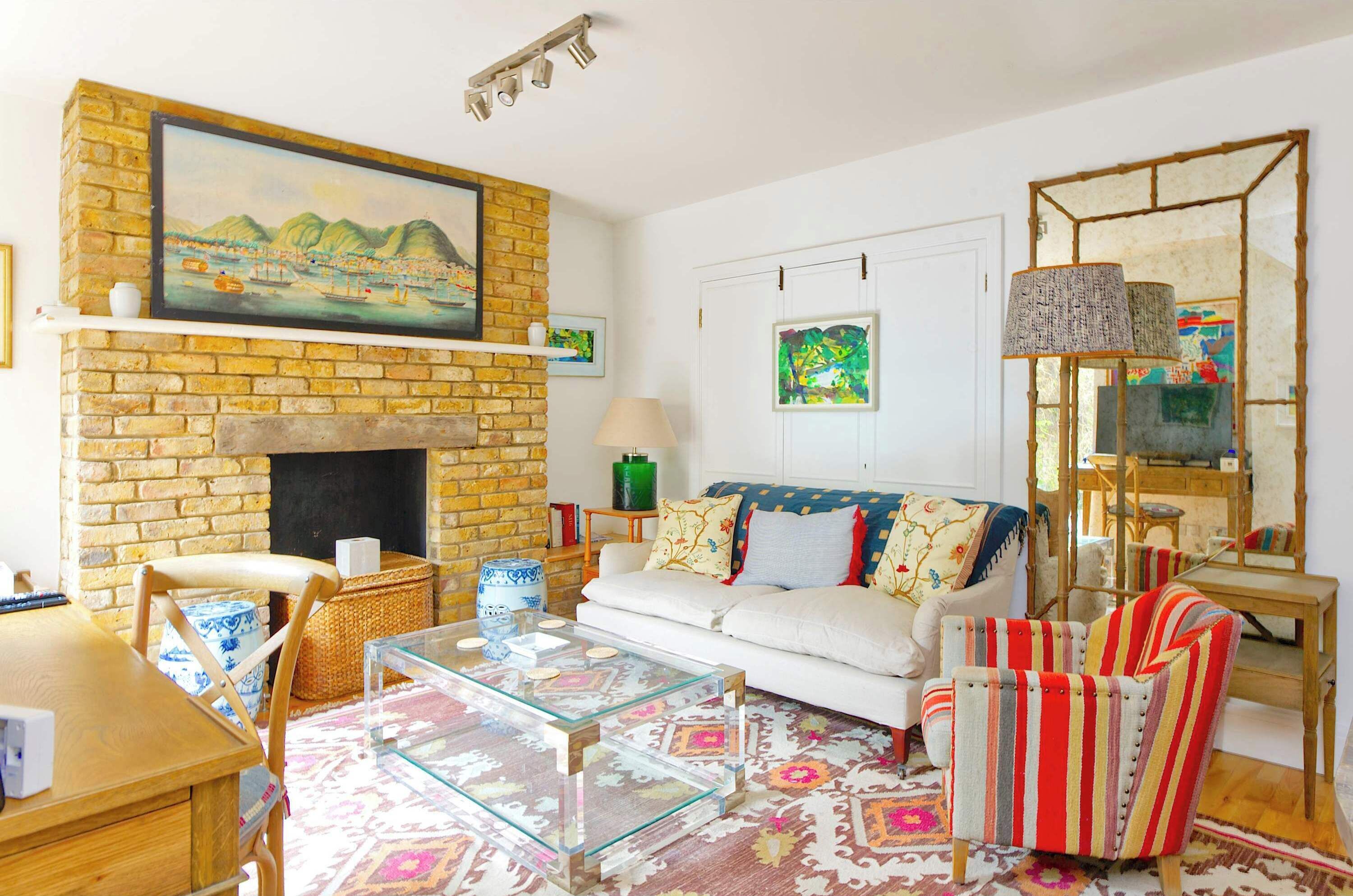 A living room with a brick fireplace, a white sofa, a glass coffee table, and striped armchairs.