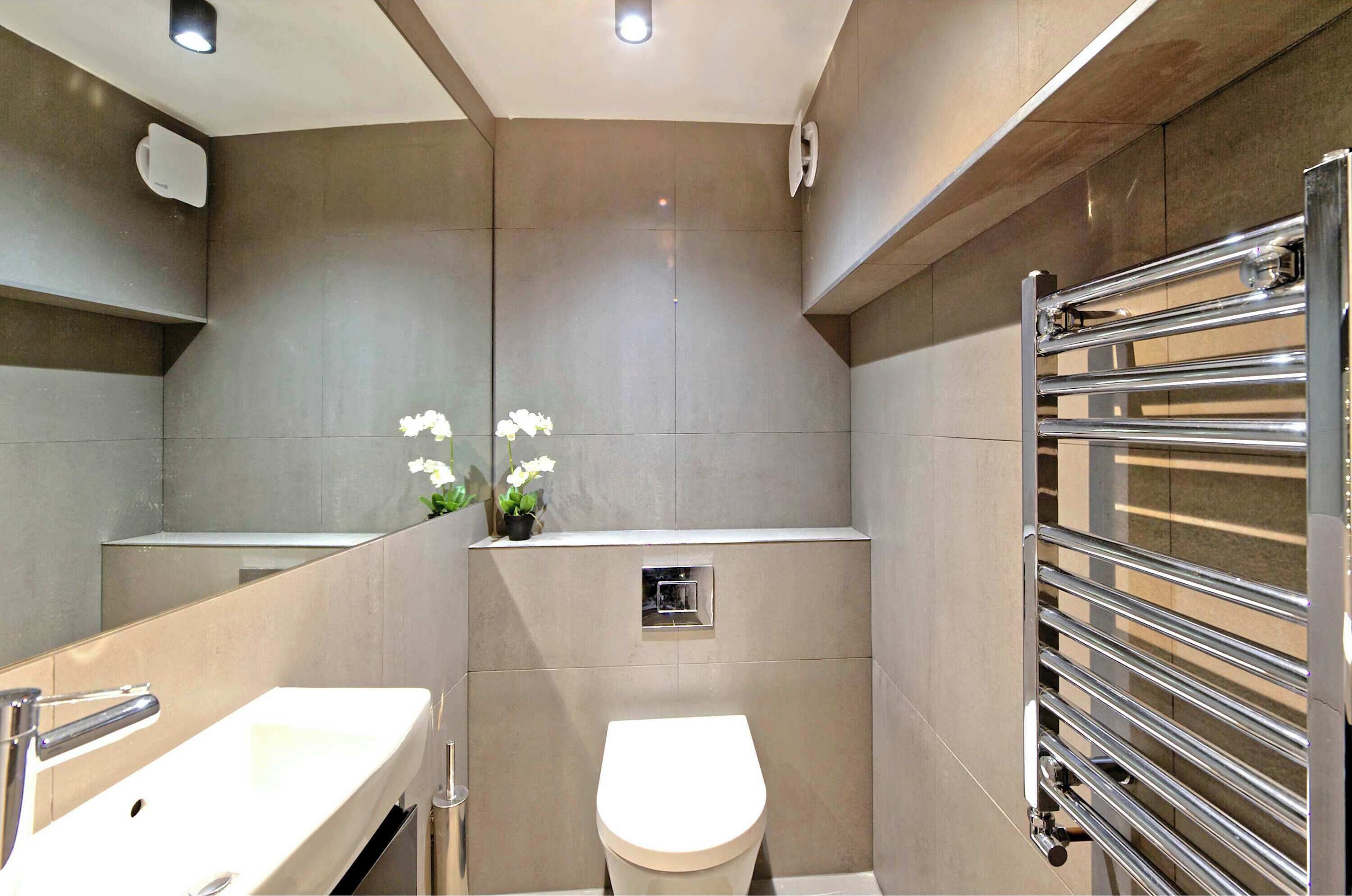 Een moderne badkamer met een grote spiegel, een wastafel, een toilet en een handdoekhouder.