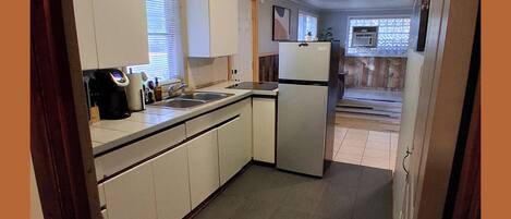 Eine kompakte Küche mit weißen Schränken, einem Kühlschrank, einer Spüle und einer Kaffeemaschine.