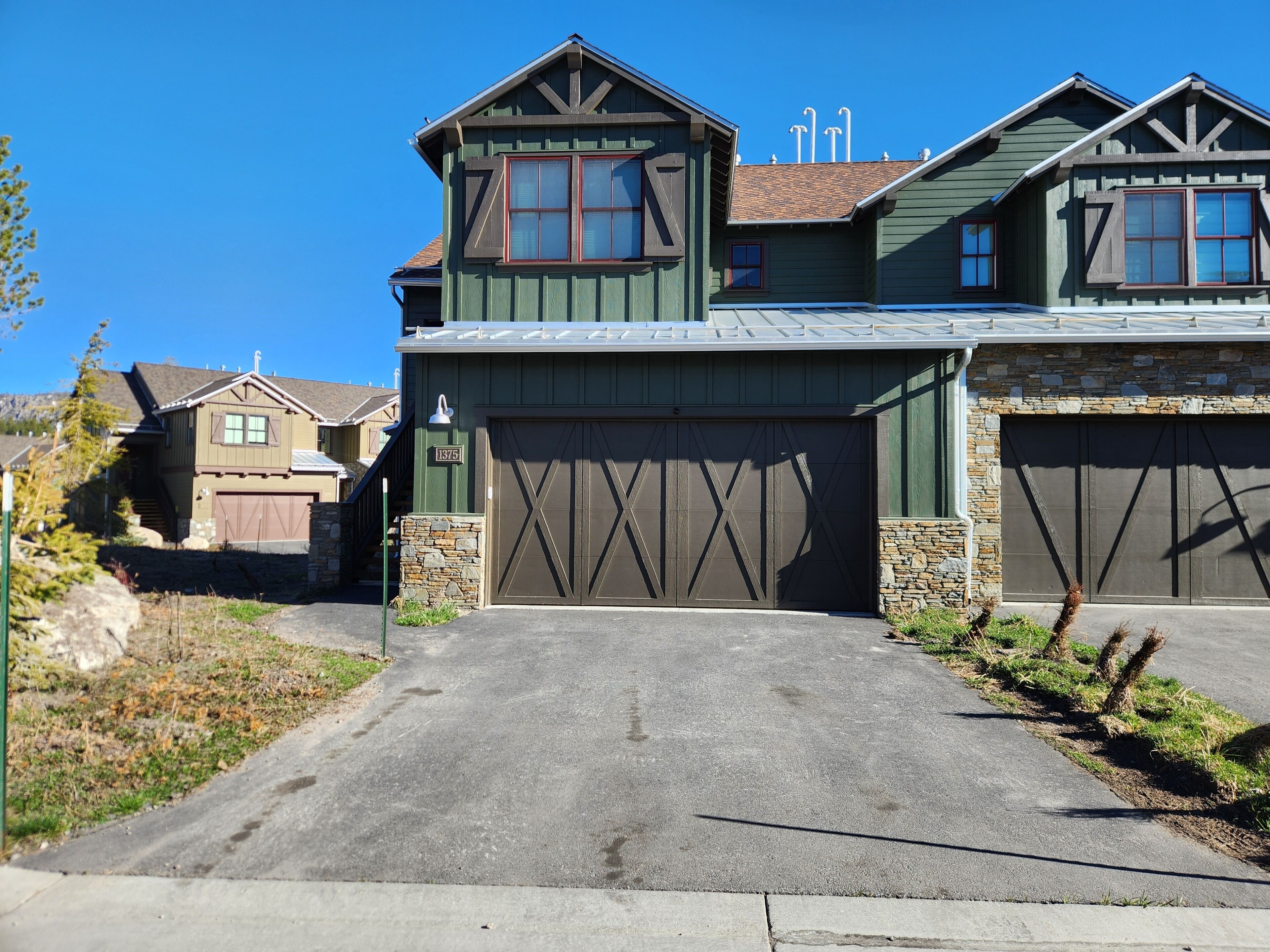 A two-story house with a garage, stone foundation, and a clear driveway.