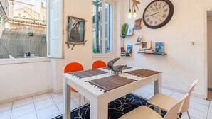 A dining area with a white table, orange chairs, a clock, and a view of the outside.