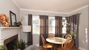 Un comedor con una mesa redonda, sillas de madera, chimenea y una ventana con cortinas.