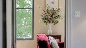 A room with a large window, a vase with flowers, a framed picture, and a small table with a cushion. - Stylish 1 Bedroom Apartment - Notting Hill (London)