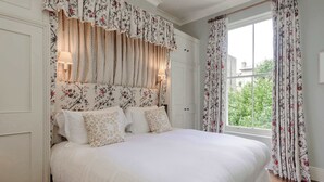 A neatly made bed with floral-patterned curtains and a view of greenery outside. - Stylish 1 Bedroom Apartment - Notting Hill (London)