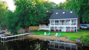 Een tweelaags huis met een steiger die uitloopt in een vijver, omgeven door groen.