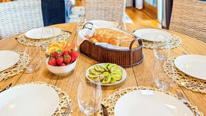 Een eetgedeelte met een houten tafel gedekt voor een maaltijd, inclusief borden, bestek en een mand met brood en fruit.