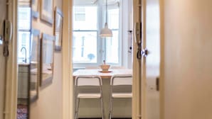 Un couloir étroit mène à un espace repas comprenant une table et des chaises, un luminaire suspendu et une fenêtre offrant une vue.