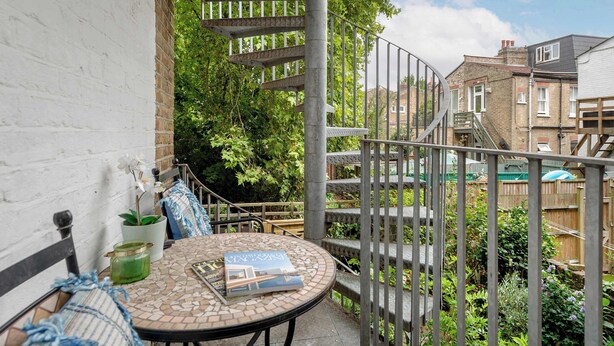 Une terrasse avec une table ronde, une chaise et un livre. Un escalier mène à une plateforme en bois.