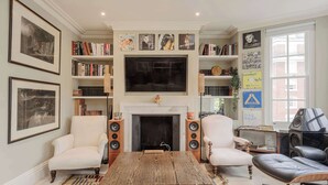 Ein Wohnzimmer mit Kamin, Bücherregalen, Fernseher und bequemen Sitzgelegenheiten.