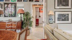Ein Zimmer mit einem Holztisch, einer Lampe, einem Topfpflanze, einem Sofa und gerahmten Bildern an der Wand.