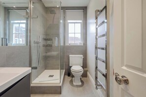 Et moderne badeværelse med bruseniche, toilet og stort spejl.