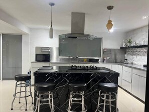 A modern kitchen with a central island, bar stools, a microwave, a stove, and a large mirror above the island. - Casa grande céntrica 19 huéspedes wifi 500Mbps (Matamoros)