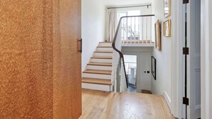 A staircase with wooden steps and a metal handrail leading to a landing with a white door and a window with curtains. - Exquisite 2 Bedroom Flat in Notting Hill (London)