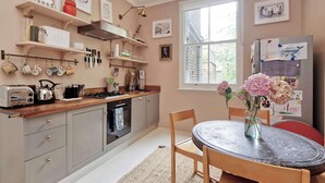 A kitchen with grey cabinets, a wooden countertop, a gas stove, and a dining area with a table and chairs. - Exquisite 2 Bedroom Flat in Notting Hill (London)