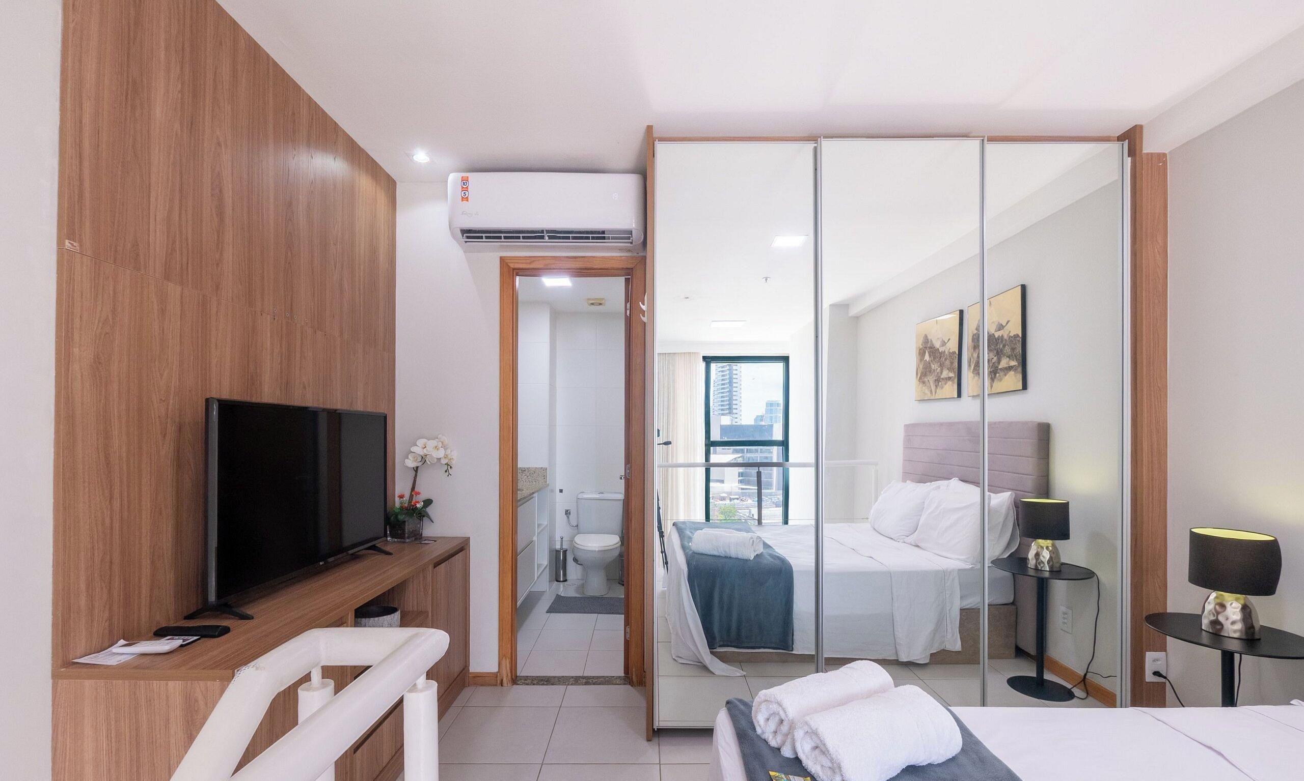 A hotel room with a bed, bedside tables, a TV, a bathroom with a toilet and sink, and a sliding door leading to a balcony.