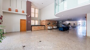 Eine geräumige Lobby mit hoher Decke, einem Empfangsbereich, einer Treppe und einer Glasreling im oberen Bereich.