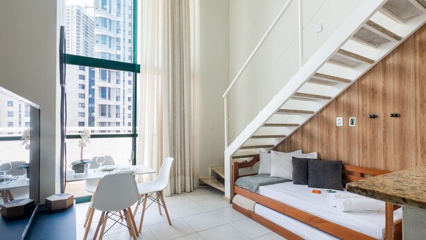 Ein modernes Hotelzimmer mit Essbereich, einem Bett mit Kissen, einer Holzwand und einer Treppe.