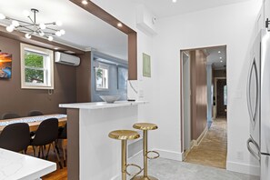 A modern kitchen with a white countertop, a dining area with a table and chairs, and a hallway leading to another room.