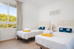 A hotel room with two beds, a window with curtains, a view of trees, and a wall with framed pictures. - Villa El Olivo - Three Bedroom Villa, Sleeps 6 (Pollença)