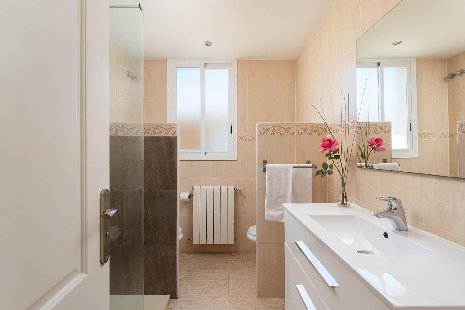 Un baño moderno con mampara de vidrio, un lavabo blanco y un espejo grande.