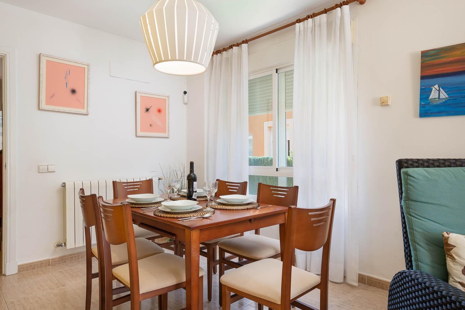 A dining area with a table set for four, chairs, a pendant light, and a view of the outside.