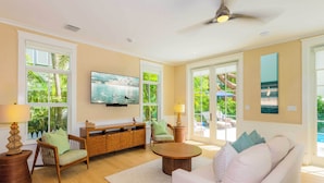 A spacious living room with a flat-screen TV, comfortable seating, a ceiling fan, and large windows offering a view of the outdoors. - Luxury Windsor, Key West Retreat- Old Town ; Pool, Gated Parking, Walk to Duval (Key West)