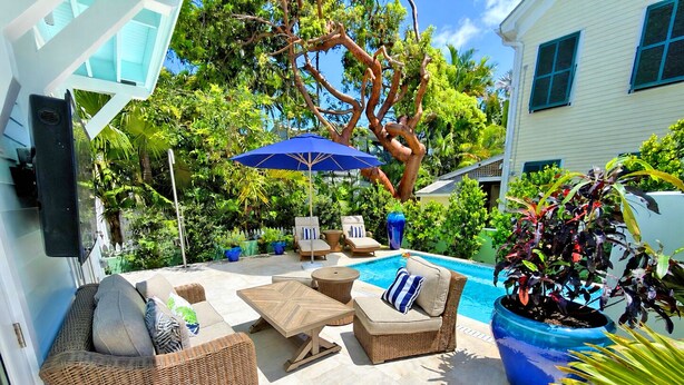 A poolside area with wicker furniture, a blue umbrella, and potted plants. - Luxury Windsor, Key West Retreat- Old Town ; Pool, Gated Parking, Walk to Duval (Key West)