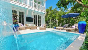 A swimming pool with lounge chairs and a TV screen, surrounded by a house with a balcony. - Luxury Windsor, Key West Retreat- Old Town ; Pool, Gated Parking, Walk to Duval (Key West)
