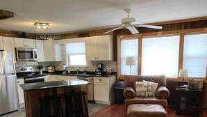 Une cuisine moderne avec des armoires blanches, un îlot central doté de tabourets, un ventilateur de plafond et un mur d’accent en pierre.