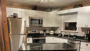 Une cuisine avec des armoires blanches, des appareils en acier inoxydable, un plancher en bois et une pancarte sur laquelle on peut lire « MAISON AU BORD DU LAC ».