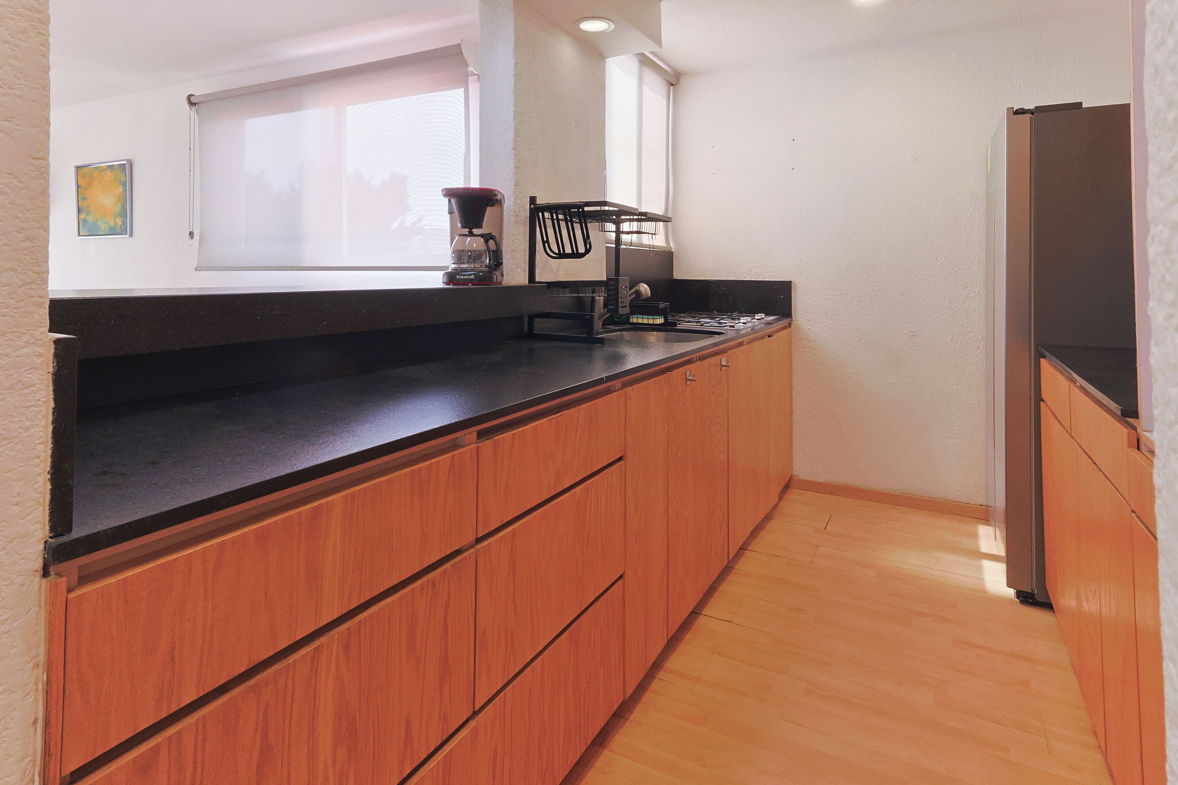 A kitchen with wooden cabinets, a black countertop, a coffee maker, and a refrigerator.