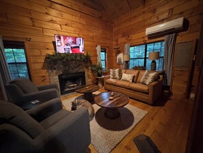 Ein gemütliches Blockhaus-Interieur mit Kamin, Fernseher, Sofa und Couchtisch.