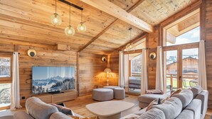 Interior d'una cabana de fusta amb un televisor gran, un sofà, otomans i una taula de menjador.
