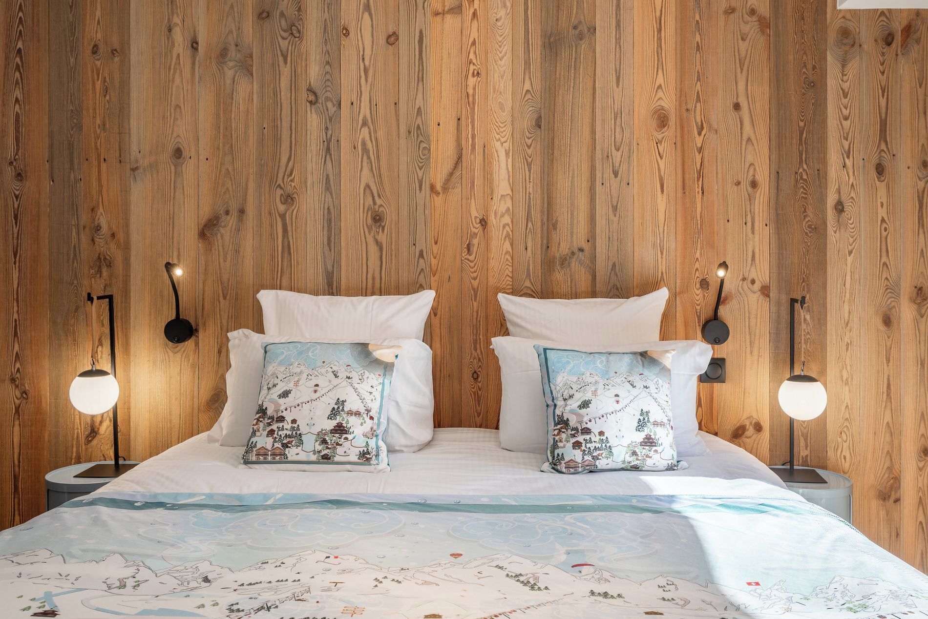 Una cama con dos almohadas, una pared de madera y dos luces fijadas a la pared.
