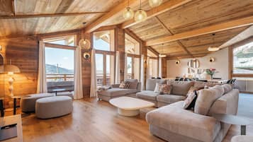 Een ruime woonkamer met houten balken, grote ramen en een moderne zithoek.