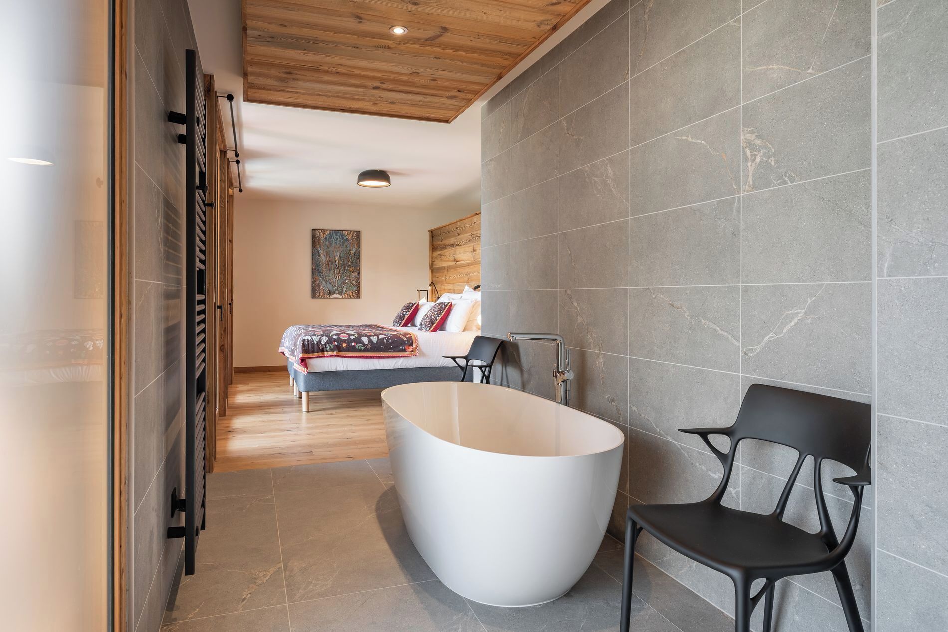 Een moderne badkamer met een vrijstaand bad, een zwarte stoel en een houten plafond.