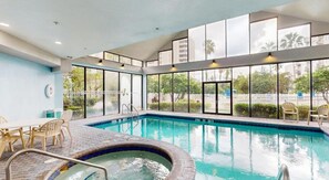 An indoor swimming pool with a hot tub, surrounded by large windows offering views of greenery and buildings. - 2BR | Free Resort Access | Minutes to Parks (Orlando)