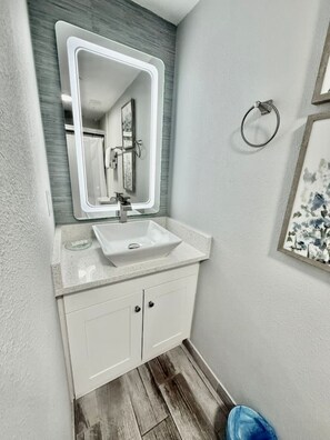 A bathroom with a white sink, a mirror, and a wooden floor. - 2BR | Free Resort Access | Minutes to Parks (Orlando)