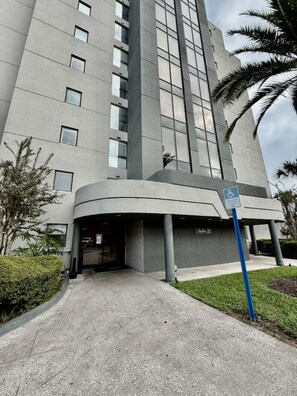 A modern building with a curved entrance, a blue handicap parking sign, and a palm tree in the foreground. - 2BR | Free Resort Access | Minutes to Parks (Orlando)
