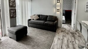 Un salon moderne avec un canapé gris, un pouf assorti et un tapis à motifs.