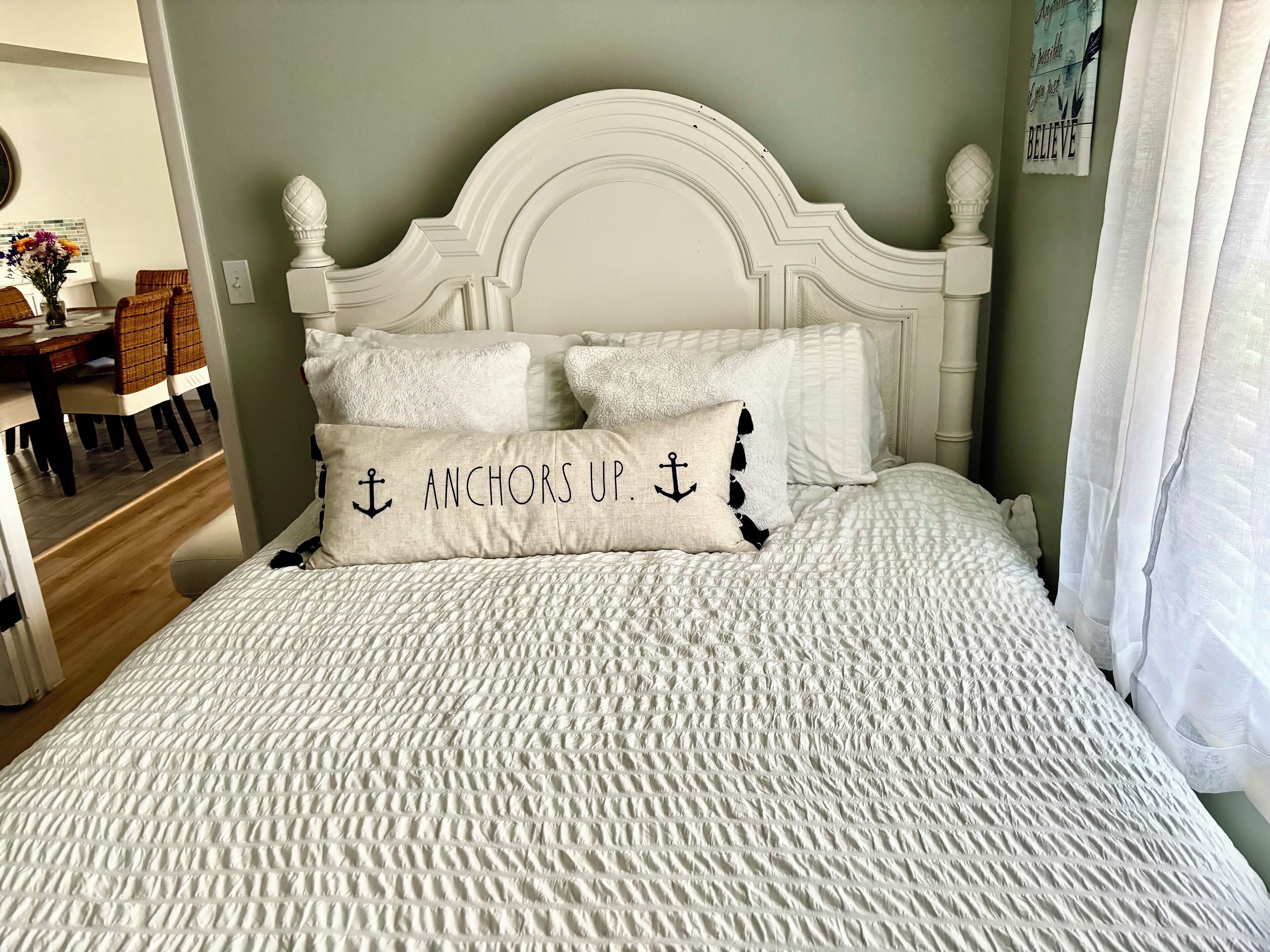 A neatly made bed with a textured white bedspread and two pillows, one with a nautical anchor design.