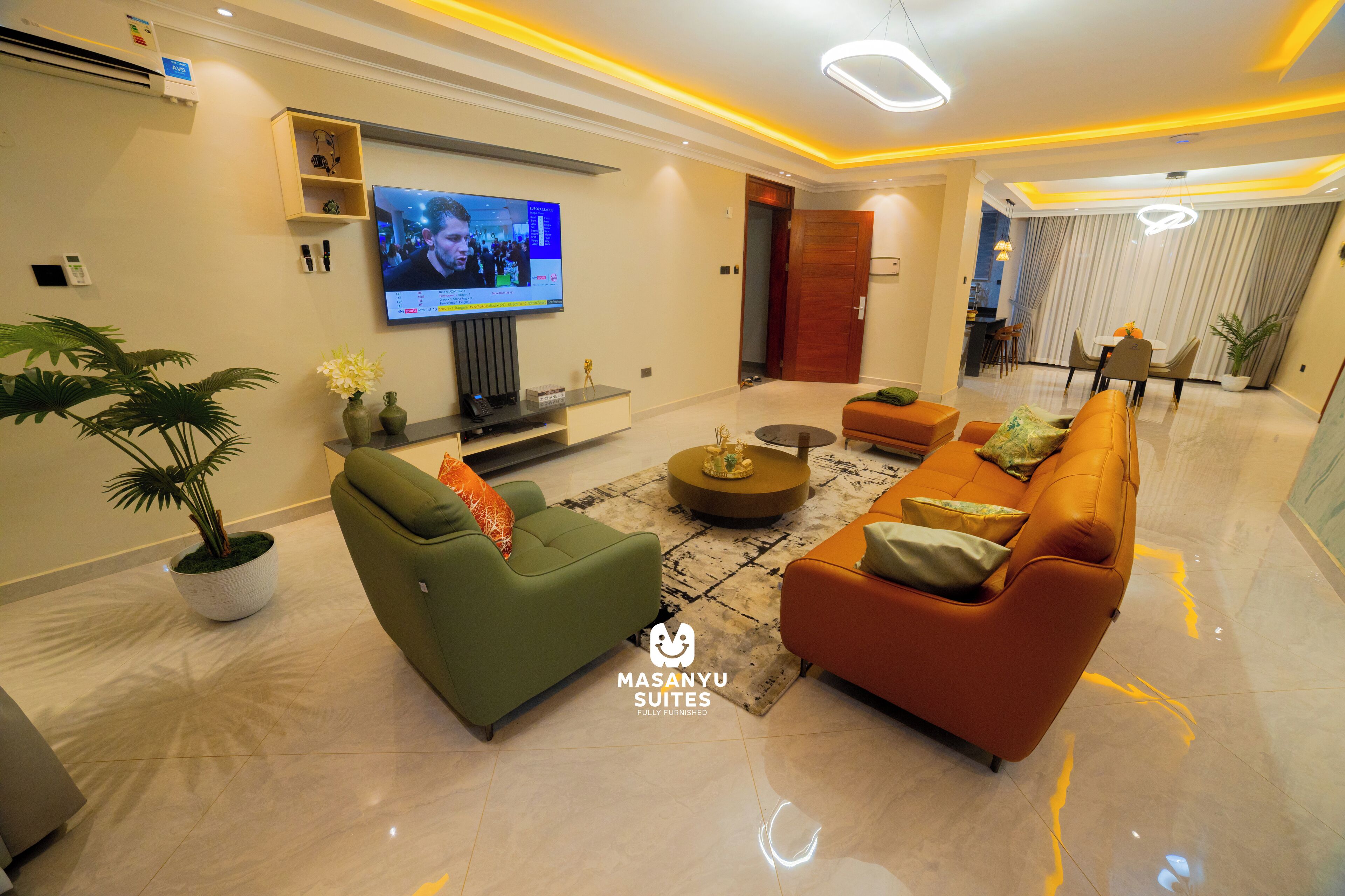 A modern living room with a flat-screen TV, sofas, a coffee table, and a potted plant.