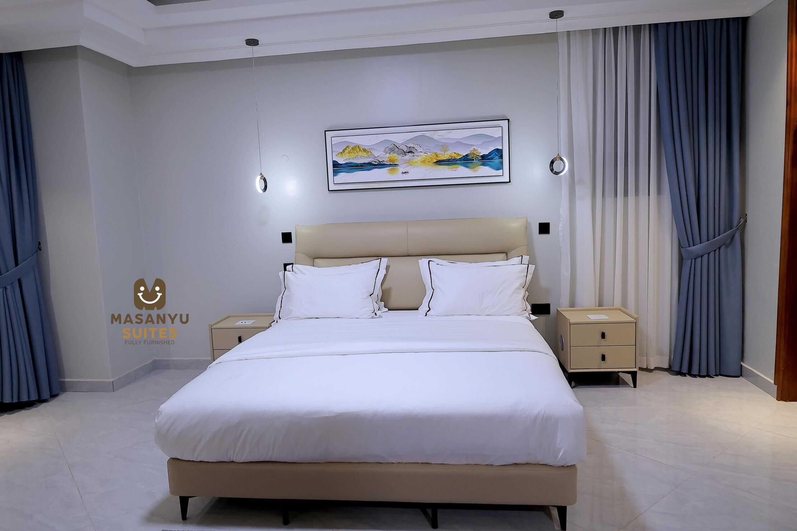 A fully furnished bedroom with a large bed, bedside tables, a wall-mounted painting, and a ceiling light fixture.