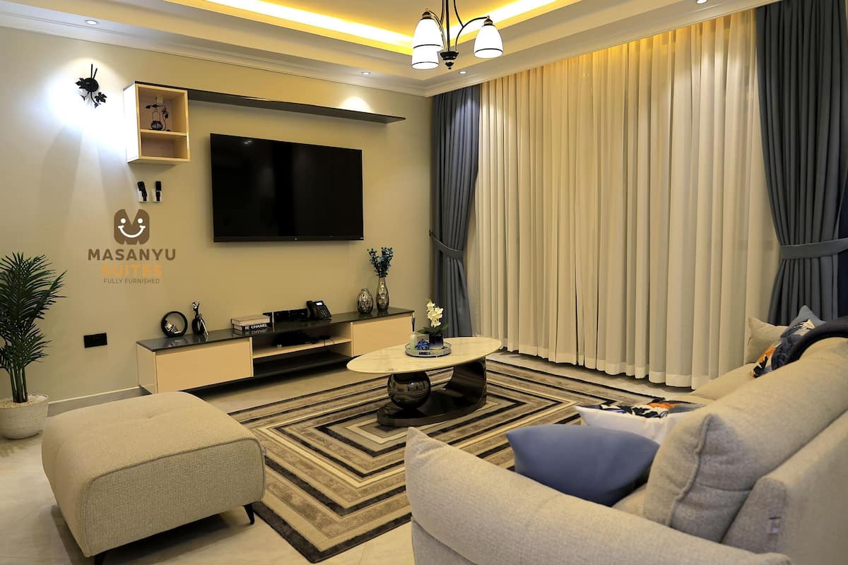 A modern living room with a flat-screen TV, a sofa, a coffee table, and a potted plant.